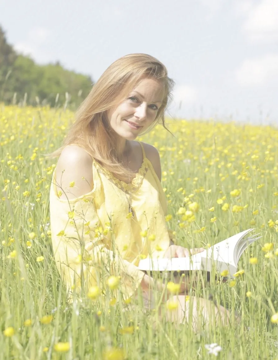 Susanne Sommer sitzt lesend in einer Wiese